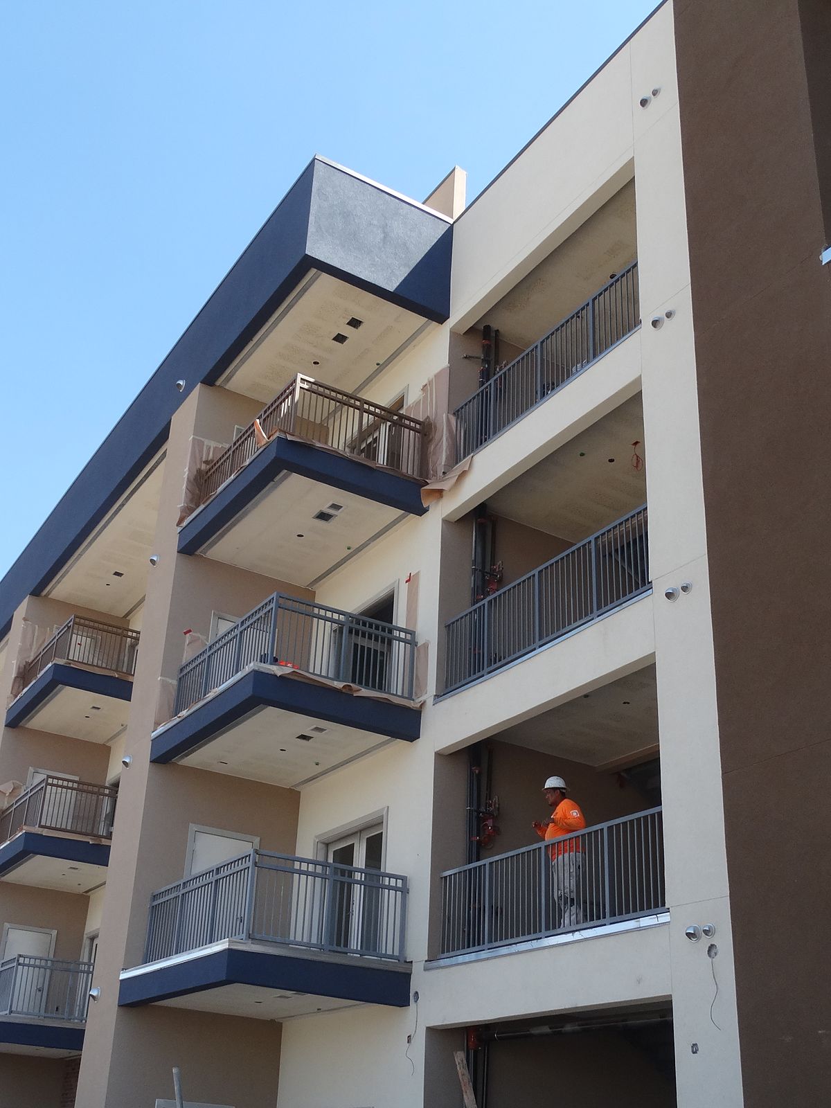 Destiny painter on a balcony of a four-story apartment building with navy and tan exterior
