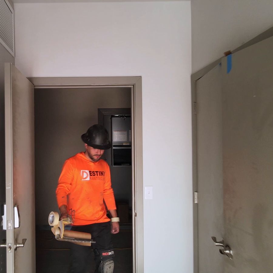 Destiny painter in a branded orange hoodie and hard hat inside a new apartment unit